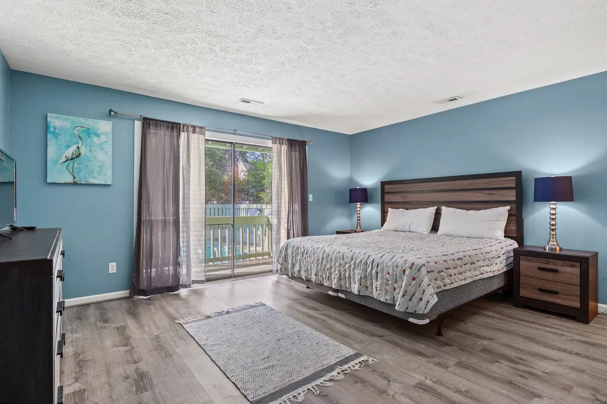 A serene and inviting bedroom featuring a comfortable king bed dressed in crisp linens, with soft curtains framing a sunlit window. The room is accented with tasteful artwork, matching nightstands, and ambient lighting, creating an atmosphere ideal for relaxation and restful sleep.