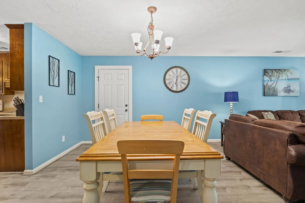 A dining area with a sturdy table set beneath a chandelier, blue accent wall with a decorative clock, and a sofa visible in the frame—ideal for family feasts, game nights, and group gatherings.