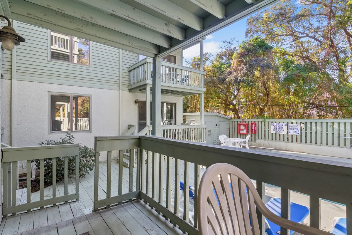 A tranquil view from a private balcony with outdoor furniture, looking out onto lush greenery and a building facade. The inviting space suggests mornings with coffee or evenings unwinding with friends, seamlessly connecting indoor comfort with outdoor relaxation.