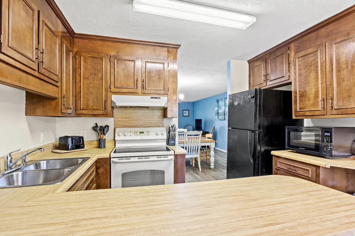 This image highlights wood cabinetry, a generous countertop, and several kitchen appliances, with the dining area nearby. The warm, homey atmosphere is evident, inviting shared cooking and meal experiences.