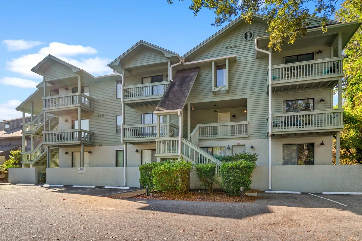 The exterior of a three-story building with multiple balconies visible, set among green landscaping. Some balconies are furnished and suggest space for gatherings or solo relaxation, while the overall scene hints at the inviting, resort-like atmosphere of the property.