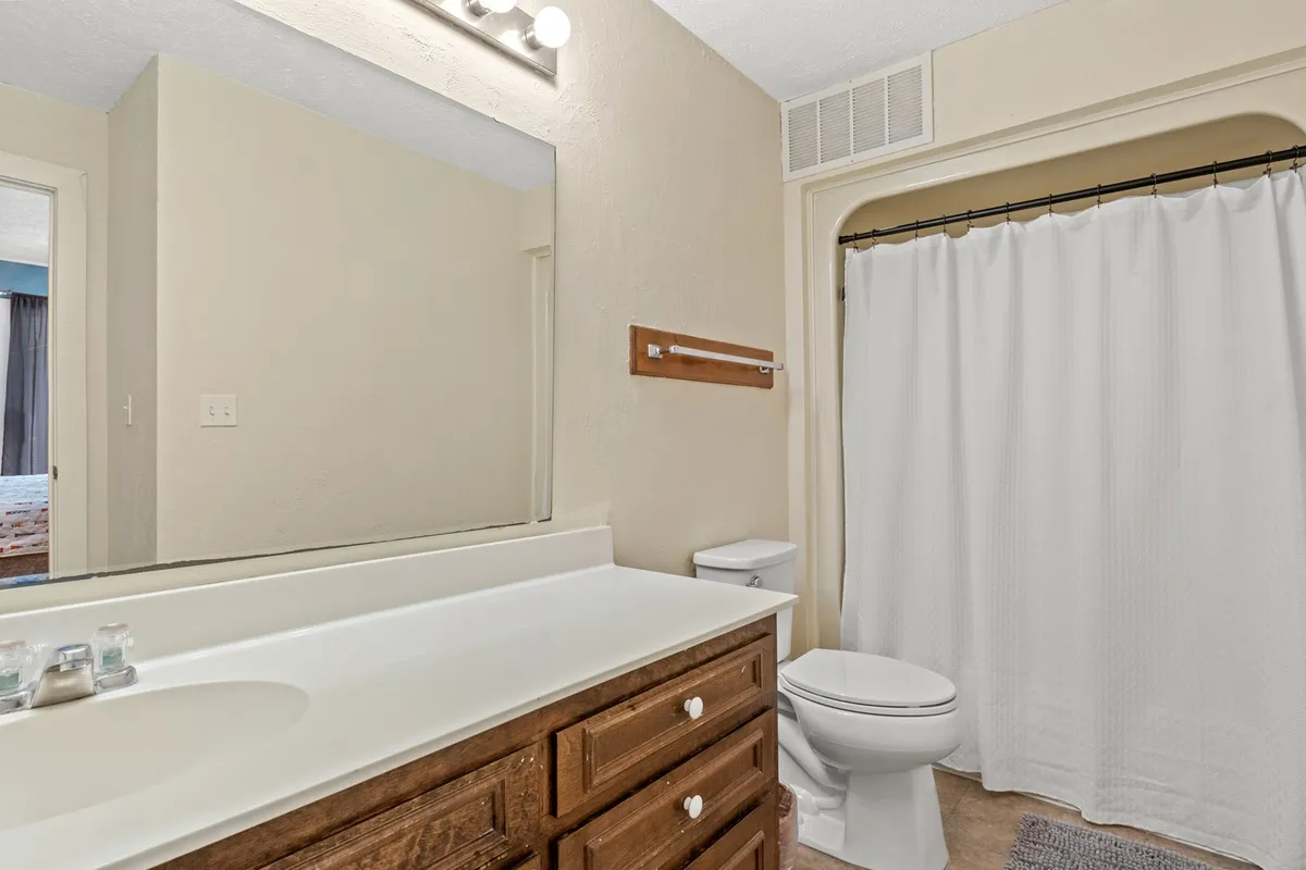 A tidy and modern bathroom featuring a vanity with a large mirror, a bright lighting fixture, and a shower with a patterned curtain. The space is organized and clean, providing a relaxing retreat for personal care routines.